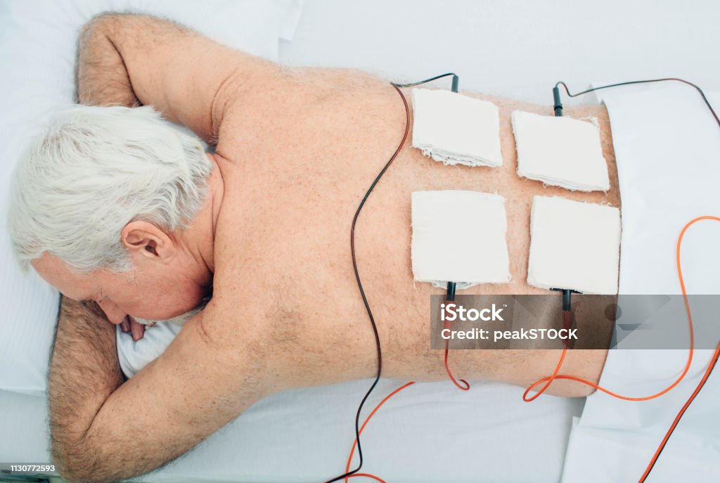 Physiotherapeutic treatment. Senior patient having ultrasound and electrotherapy treatment on his back 65-69 Years Stock Photo