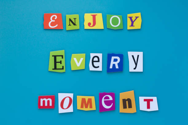 istock Inscription from cut letters - enjoy every moment on blue background. A word writing text showing enjoy every moment. Concept positive thinking for personal development. 1130789998