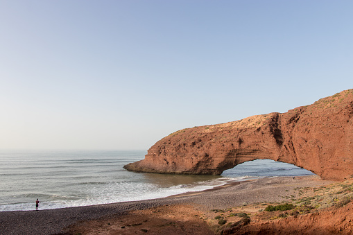 Man looking at natural stone arch over the sea