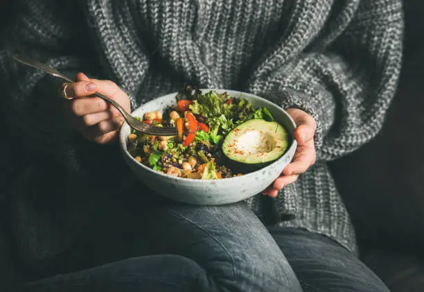Photo of Woman in sweater eating fresh salad, avocado, beans and vegetables