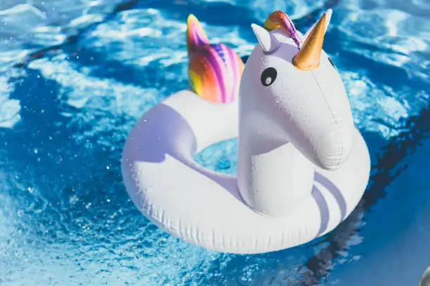 Inflatable colorful white unicorn at the swimming pool. Vacation time in the swim pool with plastic toys.Splash Water in swimming pool with sun reflection.Relaxation and fun concept