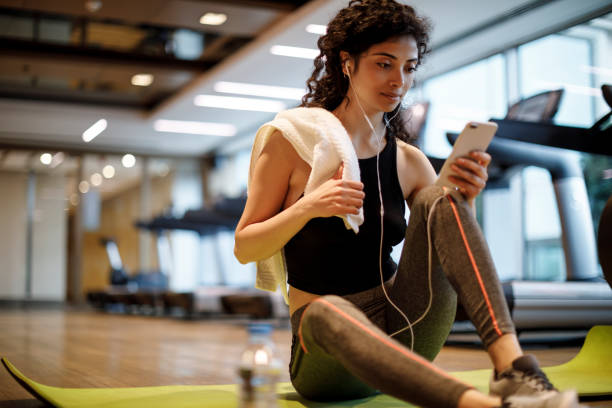 young woman listening to music over cell phone at the gym - women sweat healthy lifestyle exercising imagens e fotografias de stock