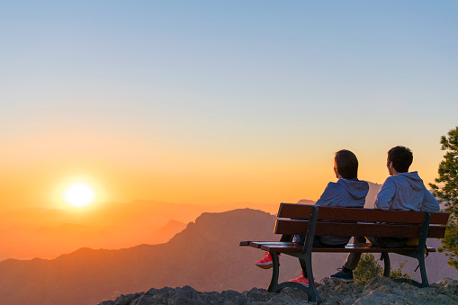 Couple sitting together watching the sunset at the top of a mountain
