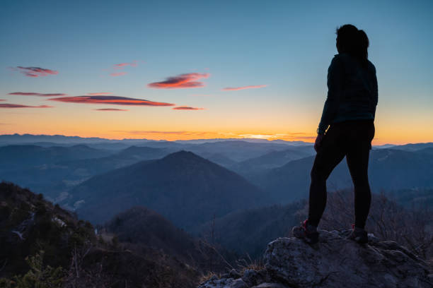 Female hiker standing on top of the hill and enjoying the view after sunset stock photo