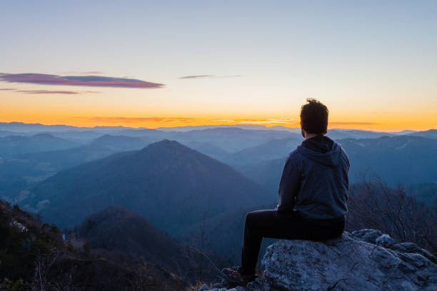 Hiker sitting on top of the hill waiting for sunrise and enjoying scenic view stock photo