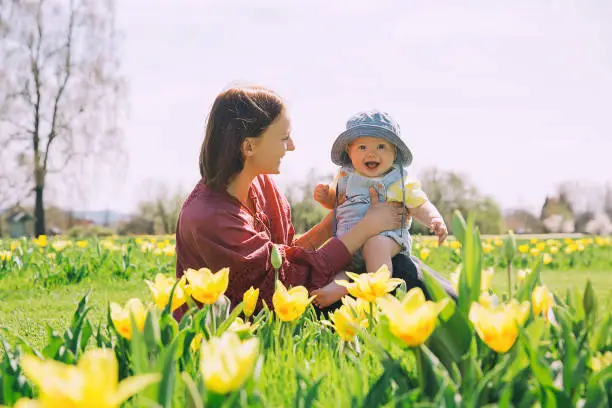 Photo of Loving mother and baby girl among yellow tulips flowers.