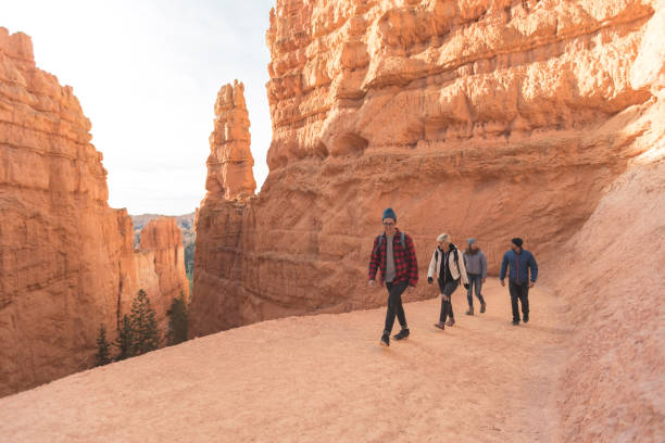 A quartet of friends in their 20s head out on a day hike through the stunning cliffs and landscapes of Utah's Bryce Canyon National Park. They are surrounded by towering, jagged pinnacles of rocks and ridges.