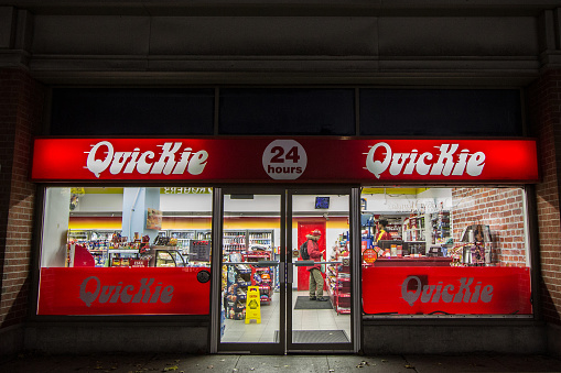 Picture of a sign with the logo of Quickie on their main store for Ottawa, Canada at night with shoppers shopping. Quickie Convenience Stores is a chain of convenience stores based in Ontario