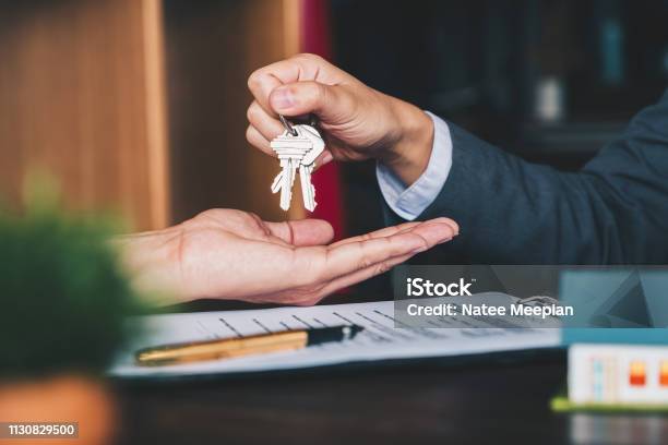 Estate Agent Giving House Keys To Woman And Sign Agreement In Office Stock Photo - Download Image Now