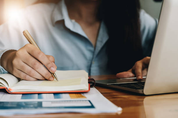 istock Close up business woman working with laptop computer and writing on a notepad with a pen in the office. Business Financial Concept 1130832146