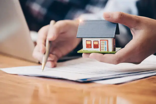 Photo of Close up real estate agent with house model hand putting signing contract,have a contract in place to protect it,signing of modest agreements form in office.Concept real estate,moving home or renting property
