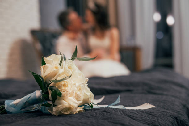 ベッドの上に白いバラの結婚式の花束、背景にぼかしカップル - honeymoon romance wedding bedroom ストックフォトと画像