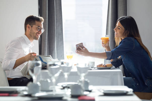 joli couple attrayant appréciant le petit déjeuner et regardant des photos dans le smartphone dans la salle à manger de l'hôtel. - hotel dining room photos et images de collection