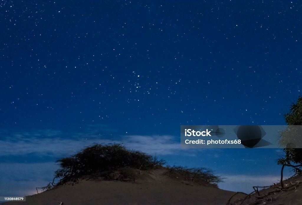 Tauro and Pleiades Over Bani Dunes, Dominican Republic Descriptive scene of the night sky with the Milky Way during the eclipse of the moon on January 21, 2019, where the Orion, Pleiades, Can Major and thousands of stars in very dark skies are clearly seen on the sand dunes of Bani in the Dominican Republic. A blue tent enhances the interest of the composition where all the elements draw attention to venturing into adventure tourism Orion Nebula Stock Photo