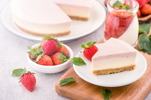 Delicious and nutritious handmade strawberry no bake frozen gradient colour fromage frais cheesecake slice with raw sarcocarp besides isolated with fair-faced gray background, copy space, close up