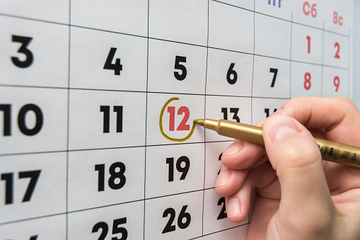 Hand with a marker on the wall calendar leads around a red holiday