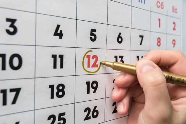 Hand with a marker on the wall calendar leads around a red holiday Hand with a marker on the wall calendar leads around a red holiday wall calendar stock pictures, royalty-free photos & images
