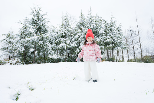 Young caucasian woman in a fur coat, white hat and gloves looking to the side against a background of snow