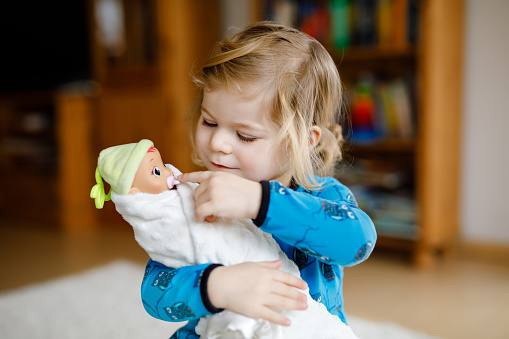 Adorable cute little toddler girl playing with doll. Happy healthy baby child having fun with role game, playing mother at home or nursery. Active daughter with toy