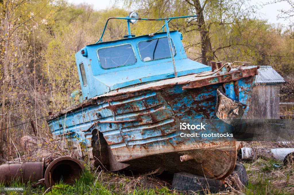 Old rusty motor boat Old blue rusty motor boat. Broken vessel on the ground. Blue Stock Photo