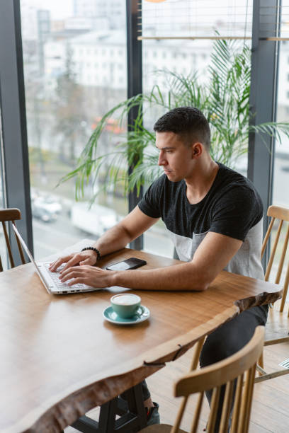 istock Freelancer work on netbook in modern coworking. Young man drinking coffee from a Cup. Programmer at remote job. Successful people, businessman in comfortable cafe. High large Windows 1130863264