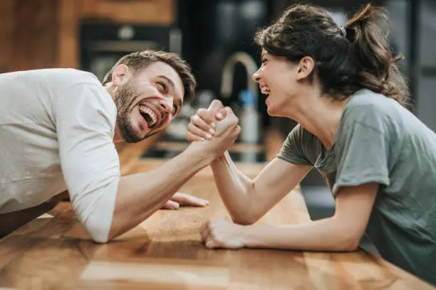 Photo of Young happy couple having fun while arm wrestling at home.