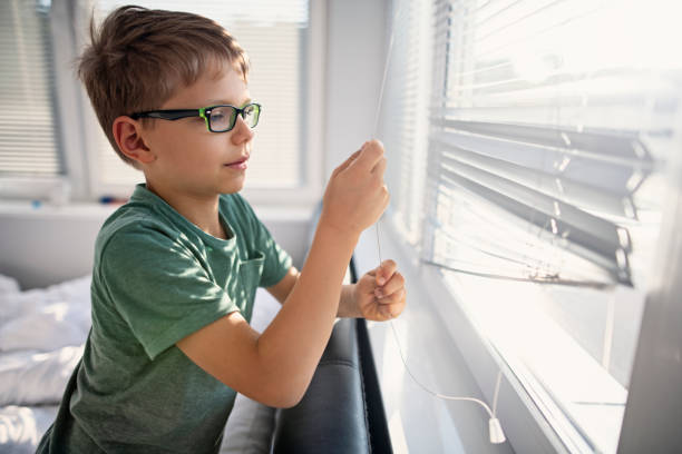 Little boy opening the blinds in the morning