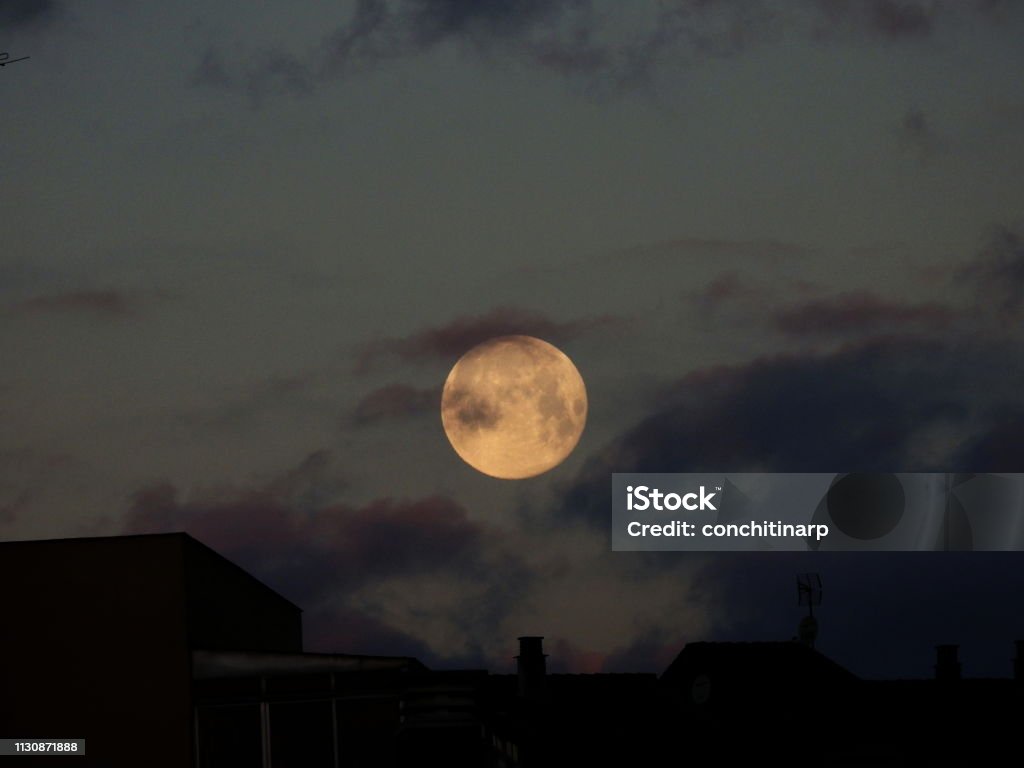 Wolf Moon on the roofs of the city Big full wolf moon over the city at dusk Full Moon Stock Photo