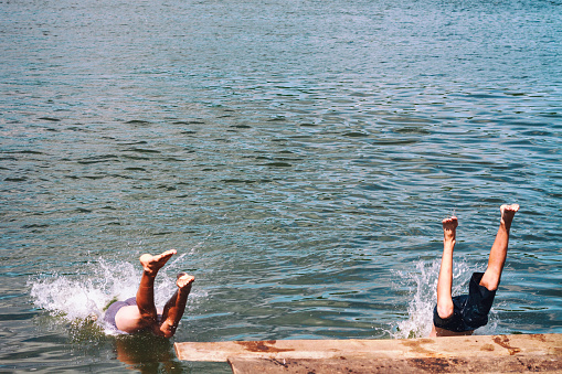 men jumping off wooden pier, feet splashing on entry to water