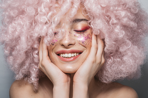 Close up studio shot of a beautiful girl wearing curly pink wig and bold make up.