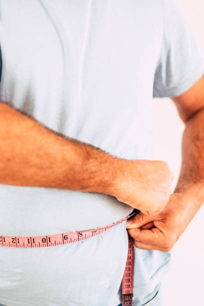 man with blue t-shirt taking measures size of the belly - fat and diet concept for people try to stay healthy and build a better body - - dieting front view vertical lifestyles imagens e fotografias de stock