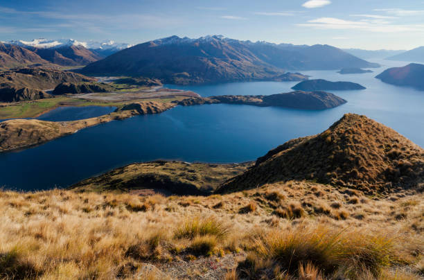 Lake Wanaka And The Southern Alps The view from Roys Peak, looking down onto Lake Wanaka and the Southern Alps beyond. foothills photos stock pictures, royalty-free photos & images