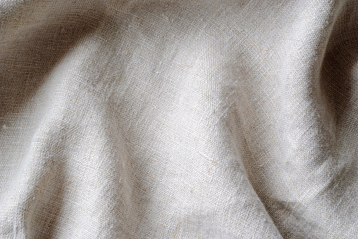 Soft folds of a natural woven linen fabric in close up detail in a full frame background texture