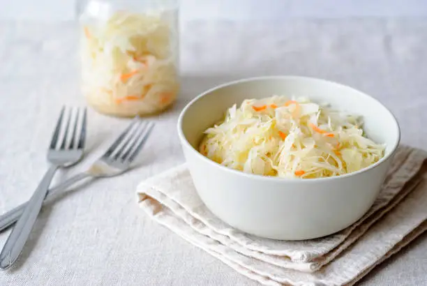 Closeup of white bowl with juicy sauerkraut served on napkin with forks