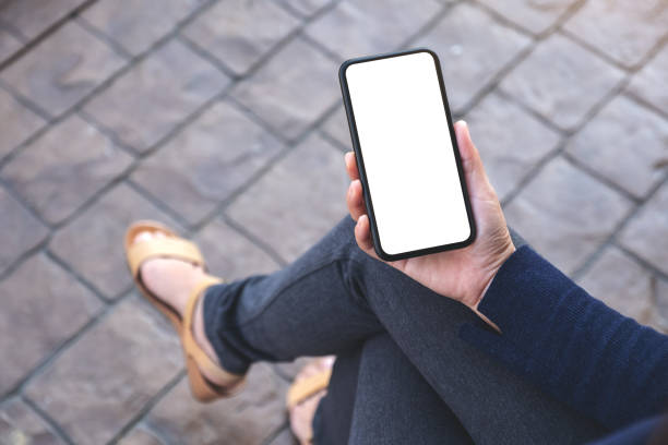 istock Top view mockup image of hand holding black mobile phone with blank white screen while sitting in the outdoors 1130894402