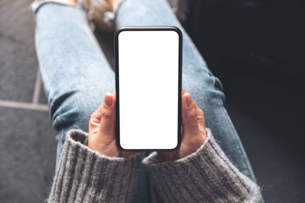istock Top view mockup image of a woman holding black mobile phone with blank desktop screen while sitting on the floor 1130894423