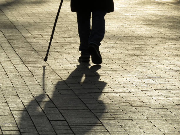 istock Silhouette of man walking with a cane, long shadow on pavement 1130896316