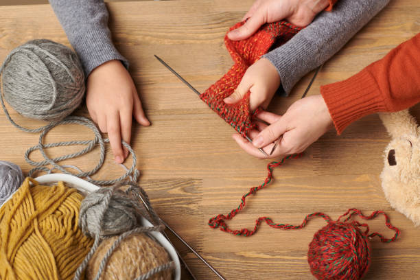 Child girl is learning to knit. Colorful wool yarns are on the wooden table. Hand closeup. Child girl is learning to knit. Colorful wool yarns are on the wooden table. Hand closeup. knitting photos stock pictures, royalty-free photos & images