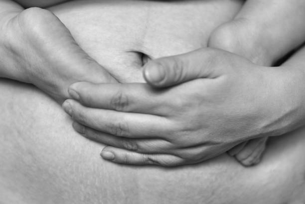 el abdomen de una mujer después de varios meses después del parto, las piernas del bebé en el vientre, la foto en blanco y negro - backwash fotografías e imágenes de stock