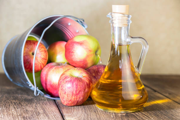 processing of an agricultural crop of red and green apples. home canning, healthy diet vegetarian food. apple cider vinegar, juice, cider in a glass jug next to a bucket of ripe fruit - slenderize imagens e fotografias de stock