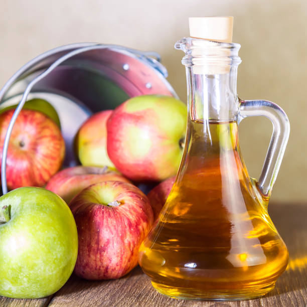 processing of an agricultural crop of red and green apples. home canning, healthy diet vegetarian food. apple cider vinegar, juice, cider in a glass jug next to a bucket of ripe fruit - slenderize imagens e fotografias de stock