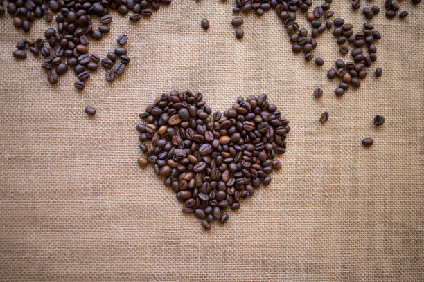 grains de café coeur forme sur toile de jute - coffee crop bean seed directly above photos et images de collection