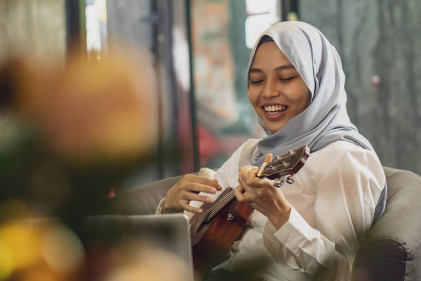 �молодая азиатская женщина играет укулеле, глядя на ноутбук - 20s acoustic guitar adult attractive female стоковые фото и изображения