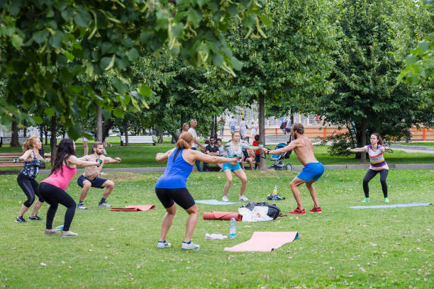 Moscow, Museon Park, July 14, 2018: Group of man and women in sportswear doing physical exercises with male coach in green summer park. Sport outdoors.
