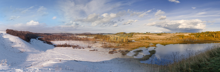Horizontal panorama of the lake valley against the blue sky. Change of seasons.