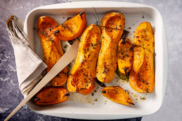 Dish of baked Butternut squashes ready to eat. Dish of freshly roasted Butternut squashes cooked until they are soft, with thyme, bay leaves and olive oil. Colour, horizontal with some copy space. roast dinner photos stock pictures, royalty-free photos & images