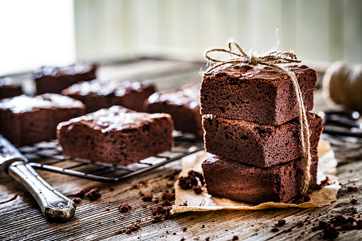 Close up view of homemade chocolate brownies shot on rustic wooden table. The brownies are tied with a rustic string and are placed on a brown craft paper. A cooling rack with brownies is at the left. Predominant color is brown. DSRL studio photo taken with Canon EOS 5D Mk II and Canon EF 100mm f/2.8L Macro IS USM.