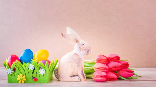 Easter nest with colorful Easter eggs, Easter bunny and red tulips against a wooden background