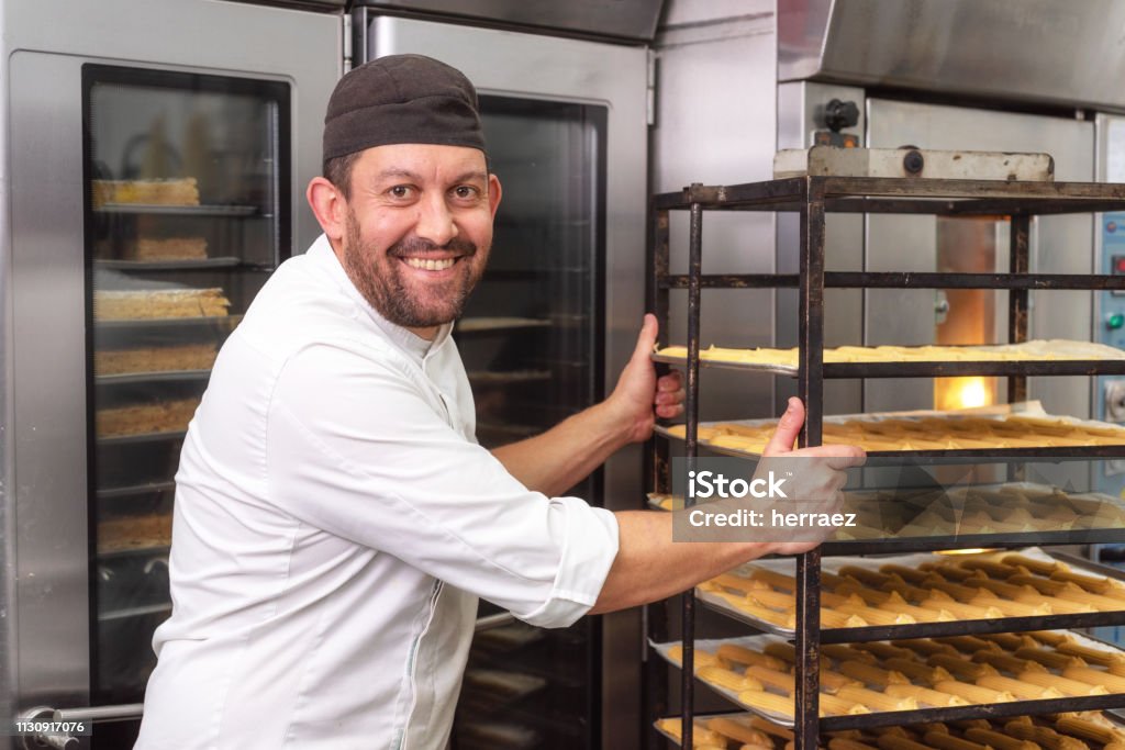 パン屋やペストリーショップでオーブンにペストリーのラックを置くベイカー。 - パン職人のロイヤリティフリーストックフォト