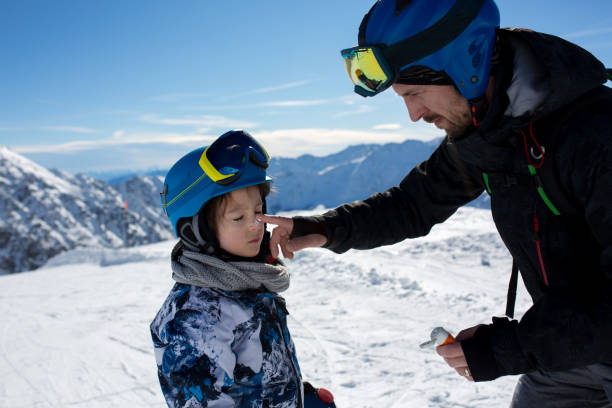 genitore, padre, mettere crema solare sul viso del bambino in cima alla montagna - skiing family winter snow foto e immagini stock
